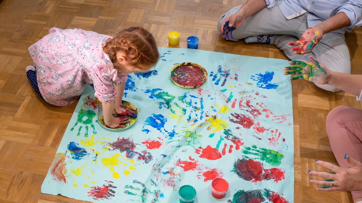 Little girl enjoying painting handprints on paper with her parents